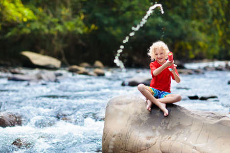 Children hiking in Alps mountains crossing river. Kids play in water at mountain in Austria. Spring family vacation. Little boy and girl on hike trail. Outdoor fun. Active recreation with children.の写真素材