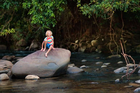 Children hiking in Alps mountains crossing river. Kids play in water at mountain in Austria. Spring family vacation. Little boy and girl on hike trail. Outdoor fun. Active recreation with children.の写真素材