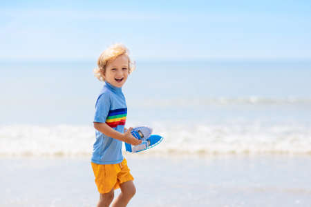 Kids playing on tropical beach. Children swim and play at sea on summer family vacation. Sand and water fun, sun protection for young child. Little boy running and jumping at ocean shore.の写真素材