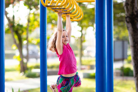 Child playing on outdoor playground in rain. Kids play on school or kindergarten yard. Active kid on...