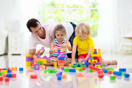 Father and kids play with colorful blocks. Dad, little boy and girl build tower at home or day care. Educational toy for young child. Construction creative game for baby or toddler kid.の写真素材