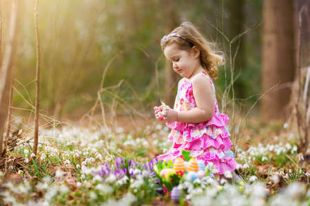 Child on Easter egg hunt in blooming garden with spring flowers. Kid with colored eggs in basket....