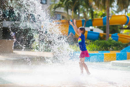 Child playing under tip bucket in water park. Kids play with splash dump bucket. Family fun in...