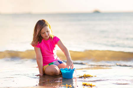 Kids playing on tropical beach. Children swim and play at sea on summer family vacation. Sand and water fun, sun protection for young child. Little girl running and jumping at ocean shore.の写真素材