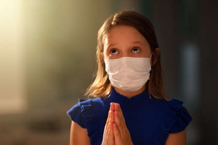 Pray for the sick. Child in face mask praying. Little girl in hospital chapel or church during...