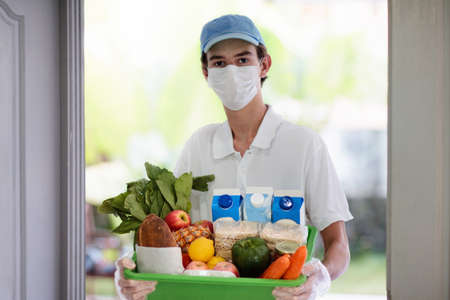 Food delivery during corona virus outbreak. Courier wearing face mask delivering grocery order in...