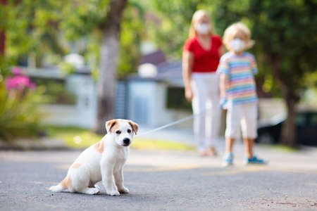 Family walking dog during virus outbreak. Woman and child wearing face mask in coronavirus lockdown and quarantine. Home animal and pet. Mother and child with puppy in pandemic or air pollution.の写真素材