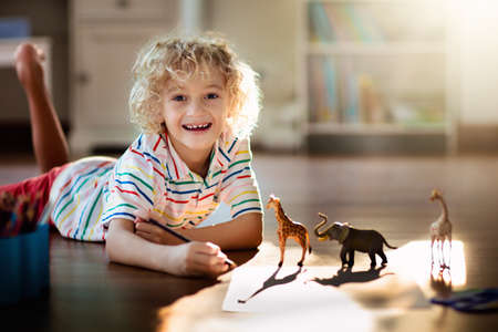 Child shadow drawing animals. Kids play at home. Fun crafts for kindergarten children. Little boy painting giraffe and elephant in sunny bedroom. Games and art during coronavirus quarantine lockdown.の写真素材