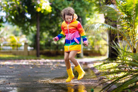 Kid playing in the rain in autumn park. Child jumping in muddy puddle on rainy fall day. Little girl...