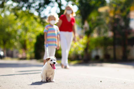 Family walking dog during virus outbreak. Woman and child wearing face mask in coronavirus lockdown and quarantine. Home animal and pet. Mother and child with puppy in pandemic or air pollution.の写真素材
