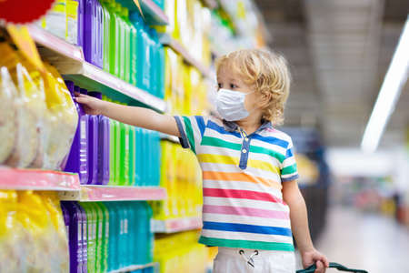 Shopping with kids during virus outbreak. Child wearing surgical face mask buying fruit in supermarket in coronavirus pandemic. Little boy buy fresh vegetable in grocery store. Covid-19 epidemic.の写真素材