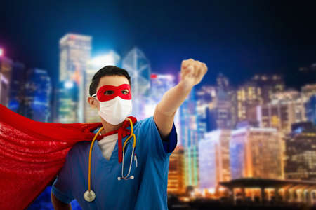 Asian doctor wearing surgical face mask in superhero cape with Hong Kong night cityscape background. Medical staff during coronavirus outbreak in Asia city. Super hero power for hospital personal.の写真素材