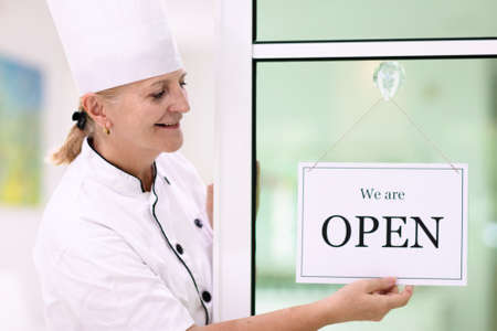 Cafe opening after lockdown. Open sign on front door of restaurant or grocery store. Waiter in apron...