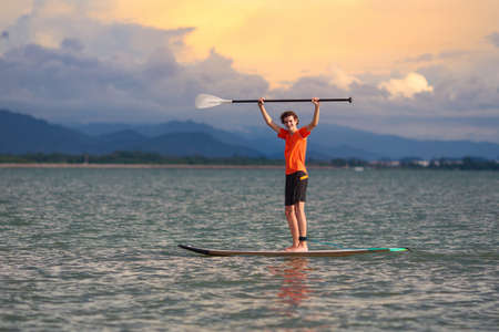 Young man on stand up paddle board. Water fun and beach sport. Healthy outdoor sports for summer vacation on tropical island. Holiday activity. Fit teenager boy training. Surfer exercising.の写真素材