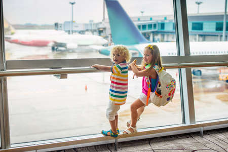 Kids at airport. Children look at airplane. Traveling and flying with child. Family at departure gate. Vacation and travel with young kid. Boy and baby before flight in terminal. Kids fly a plane.の写真素材