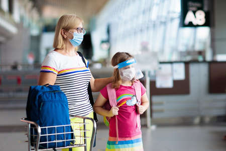 Family in airport in face mask and shield. Virus outbreak. Coronavirus and flu pandemic. Safe travel with young child and baby. Mother and kids boarding airplane in surgical masks.の写真素材