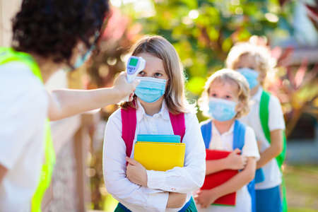 Temperature screening and medical check at school. Child in face mask in class in covid-19 outbreak. Teacher with thermometer at preschool entrance. Social distancing. Coronavirus prevention.の写真素材