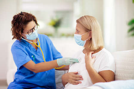 Doctor examining sick patient in face mask. Ill woman in health clinic for test and screening. Home treatment of virus. Coronavirus pandemic. Covid-19 outbreak. Woman coughing, having chest pain.の写真素材