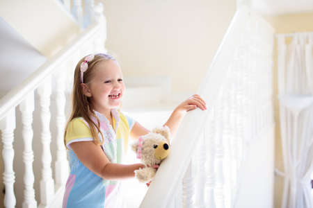 Kid walking stairs in white house. Little girl playing in sunny staircase. Family moving into new home. Child climbing steps of modern stairway. Foyer or living room interior. Home safety for toddler.の写真素材