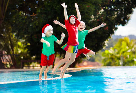 Christmas vacation on tropical island. Kids in Santa hat playing in swimming pool on family Xmas vacation. Winter holidays at the beach. Travel with children. Boy and girl swim. Merry Christmas card.の写真素材