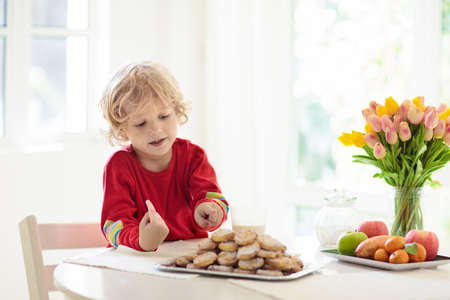 Child eating breakfast. Kid drinking milk with fresh homemade cookies. Baking and cooking with kids. Little boy with fruit bowl and pastry for family lunch at home. Dining room with big window.の写真素材