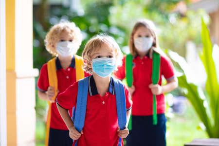 School child wearing face mask during corona virus and flu outbreak. Boy and girl going back to school after covid-19 quarantine and lockdown. Group of kids in masks for coronavirus prevention.