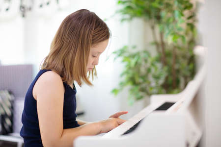 Child playing piano. Kids play music. White digital piano for kids lessons. Little boy practicing for music school study. Musical instrument for children. Classical arts education.の写真素材