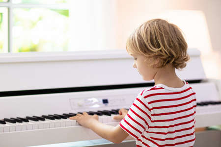 Child playing piano. Kids play music. Classical education for children. Art lesson. Little boy at white digital keyboard. Instrument for young student. Music class in school or at home.の写真素材