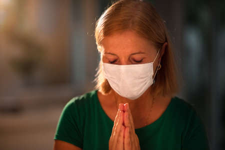 Pray for XXX. Woman in face mask praying. Senior patient in hospital chapel or church during...