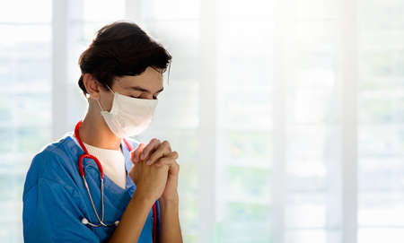 Doctor in face mask praying for XXX. Medical staff in hospital chapel or church during coronavirus outbreak. Virus pandemic. People pray. Nurse saying a prayer for sick patient.の写真素材