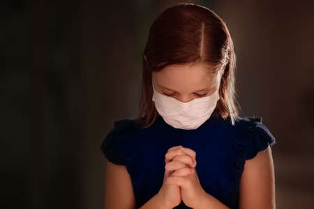 Pray for XXX. Child in face mask praying. Little girl in hospital chapel or church during coronavirus outbreak. Virus pandemic. Kids worship. Children say a prayer for sick patient.の写真素材
