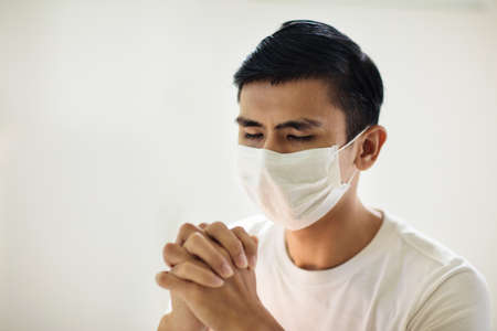 Pray for XXX. Asian man in face mask praying. Patient in hospital chapel or church in coronavirus outbreak. Virus pandemic. People worship. Nurse saying a prayer for sick XXX patient.の写真素材