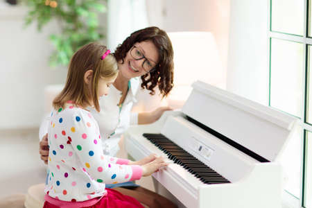 Child playing piano. Kids play music. Classical education for children. Art lesson. Little girl at white digital keyboard. Instrument for young student. Music class in school or at home.の写真素材