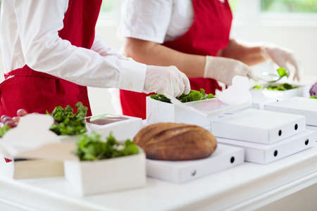 Food takeaway in restaurant in coronavirus outbreak. Cafe staff in face mask and shield cooking...