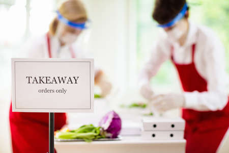 Food takeaway in restaurant in coronavirus outbreak. Cafe staff in face mask and shield cooking...