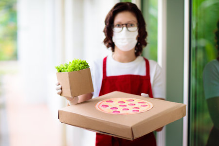 Food delivery in lockdown. Take away food during coronavirus outbreak. Restaurant owner in face mask holding pizza and salad box. Stay home and be safe. Meal order in covid-19 pandemic.の写真素材