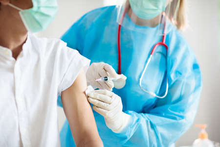 Coronavirus vaccine injection at doctor office. Covid-19 vaccination in hospital. Doctor in protective suit examining patient. Nurse with syringe. Asian man getting corona virus shot.の写真素材