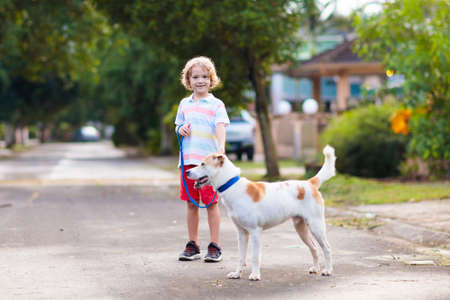 Child walking dog. Kid playing with cute puppy. Little boy running with his pet. Children play in suburban neighborhood street. Animal friends. Friendship and love.の写真素材