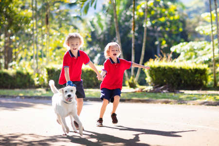 Child walking dog. Kid playing with cute puppy. Little boy running with his pet. Children play in suburban neighborhood street. Animal friends. Friendship and love.の写真素材