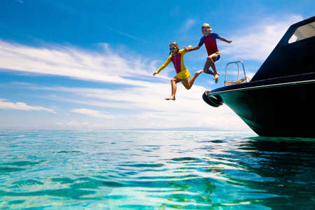 Kids jump into sea. Yacht vacation with child on exotic tropical island with crystal clear water. Beach and swim fun. Sailing and cruise with children. Summer holiday on boat. Little boy swimming.の写真素材