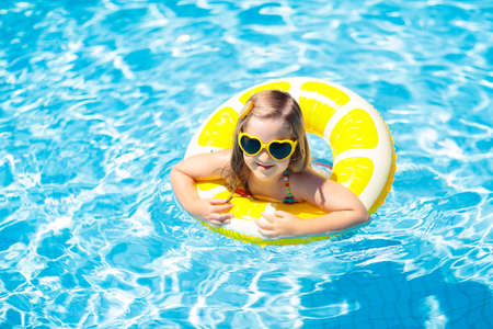 Child in swimming pool on inflatable yellow lemon ring. Little girl learning to swim with orange...