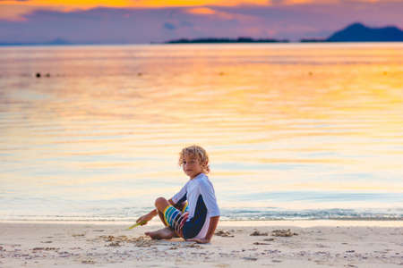 Child playing on ocean beach. Kid jumping in the waves at sunset. Sea vacation for family with kids. Little boy on tropical beach of exotic island on summer holiday. Sunset view. Sand and water fun.の写真素材