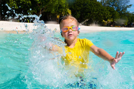 Kids playing on tropical beach. Children swim and play at sea on summer family vacation. Sand and water fun, sun protection for young child. Little boy running and jumping at ocean shore.の写真素材