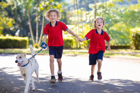 Child walking dog. Kid playing with cute puppy. Little boy running with his pet. Children play in suburban neighborhood street. Animal friends. Friendship and love.の写真素材
