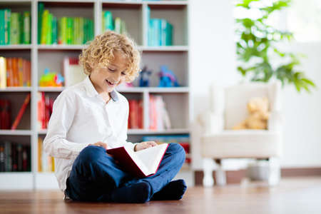 Child reading book. Kids read. Little boy at a colorful bookshelf doing homework for school. Student...