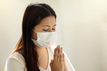 Pray for patient. Asian woman in face mask praying for infected family member. Patient in hospital church in virus outbreak. People worship. Nurse saying a prayer for sick person.の写真素材