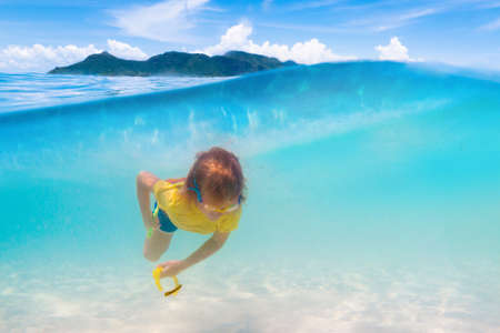 Kids swimming on tropical beach. Children swim and play at sea on summer family vacation. Sand and water fun, sun protection for young child. Little boy underwater, split imageの写真素材