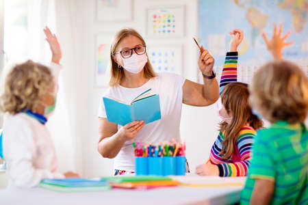 Teacher in class, school child in face mask during virus and flu outbreak. Boy and girl back to school after  quarantine and lockdown. Group of kids in masks for virus prevention.の写真素材