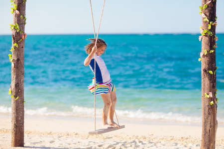 Child on swing. Kid swinging on tropical beach. Travel with young children. Summer family vacation on exotic island. Kids play on sea shore. Little girl playing in luxury resort.の写真素材