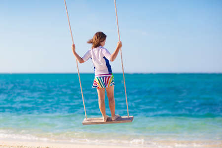 Child on swing. Kid swinging on tropical beach. Travel with young children. Summer family vacation on exotic island. Kids play on sea shore. Little girl playing in luxury resort.の写真素材